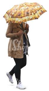 woman in a beige coat walking under an umbrella and listening to music