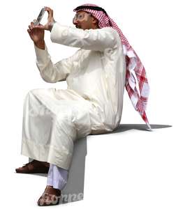 arab man in a thobe sitting and taking a picture