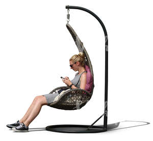 woman sitting in a hanging chair and looking at her phone