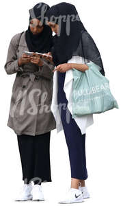 two young muslim women standing and looking at their phones
