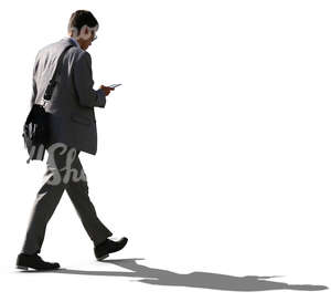 backlit businessman walking while looking at his phone