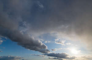 daytime sky with sun shining between grey clouds