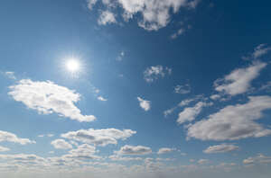 daytime sky with sun and small white clouds