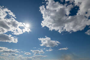 daytime sky with sun shining between white clouds