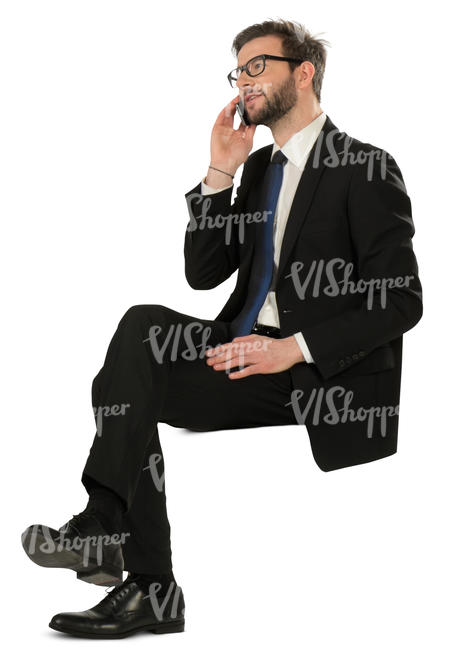 man in a black suit sitting and talking on a phone