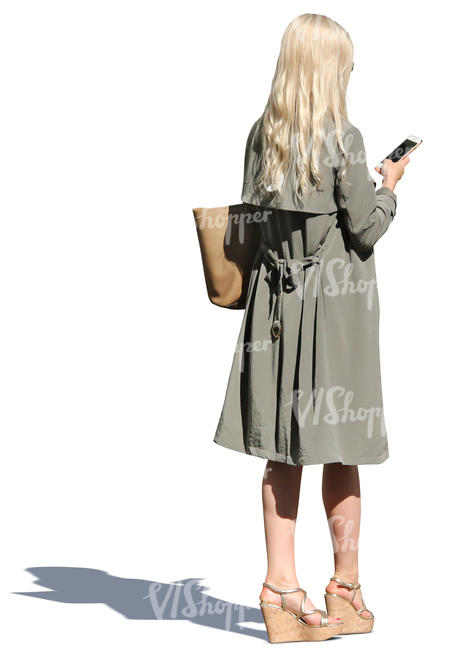 woman in a light trenchcoat standing and texting