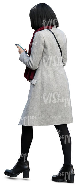 woman in a light grey coat walking and looking at her phone