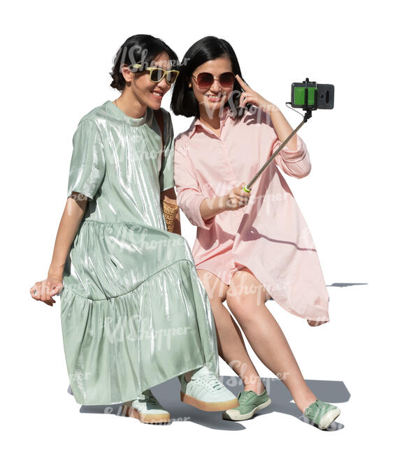 two cut out young asian women sitting and taking a selfie