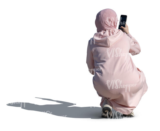 woman wearin g a pink abaya and hijab squatting and taking a picture