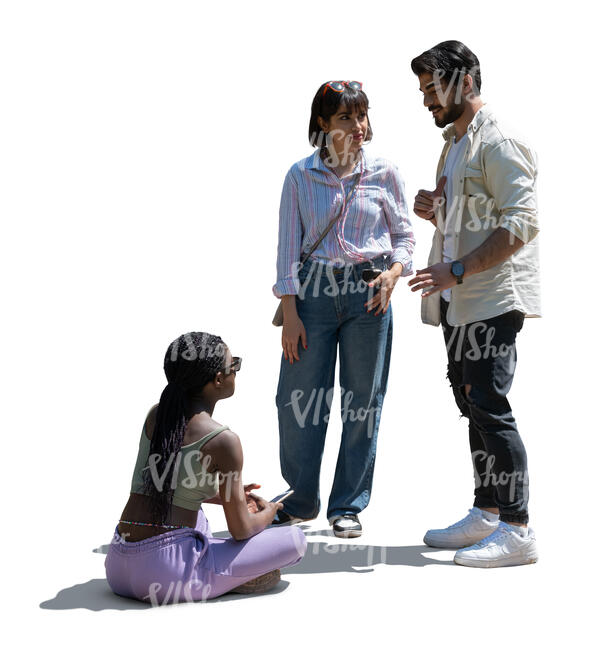 woman sitting on the ground and talking to two friends standing