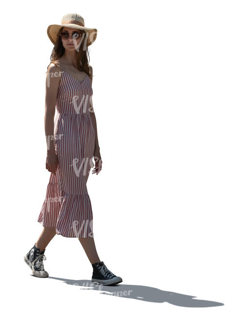 backlit young woman in a dress and wearing a hat walking