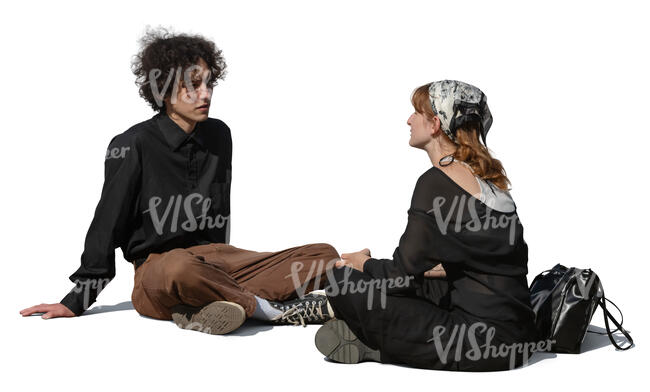 two young people sitting on the ground and talking