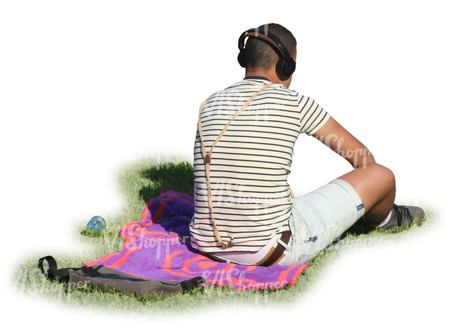 man with headphones sitting in a park on a blanket