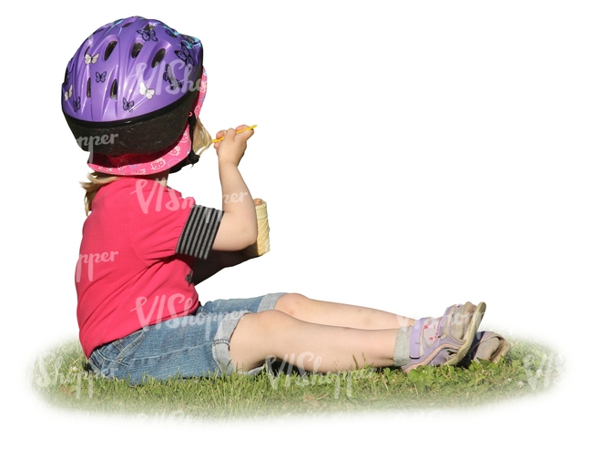 young girl with a helmet sitting on the grass and eating icecream
