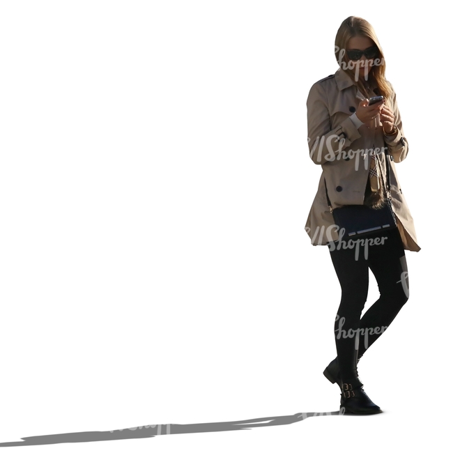 backlit woman in a trenchcoat walking phone in hand