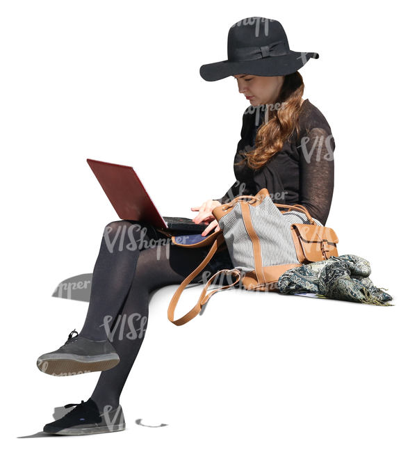 woman with a large hat sitting and working with a laptop.