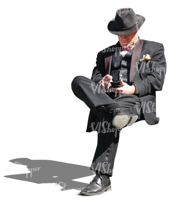man in a black formal suit sitting and looking at his phone