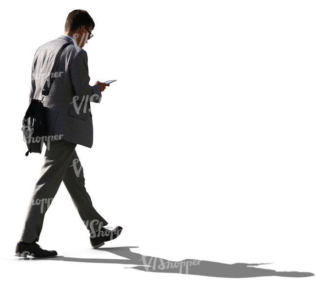 backlit businessman walking while looking at his phone