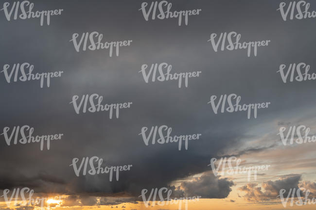 sun setting behind large grey cloud